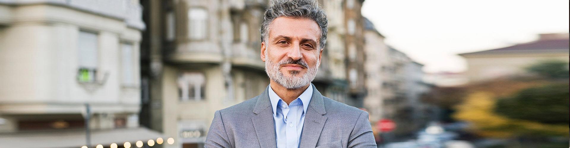 Contas à vista - Hombre de negocios con traje y smartwatch con los brazos cruzados en una ciudad