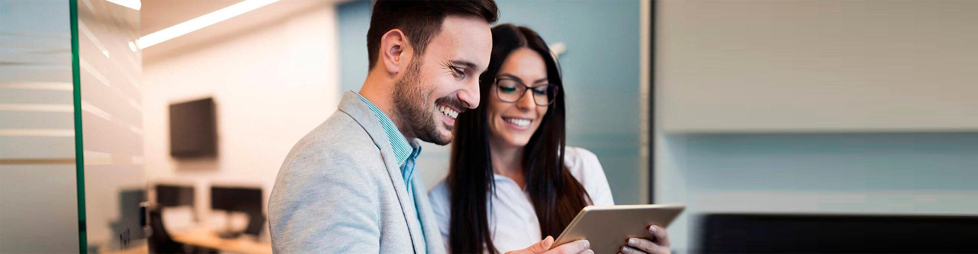 Cash Pooling - Homem de traje sorrindo junto a uma mulher de óculos sorrindo no escritório